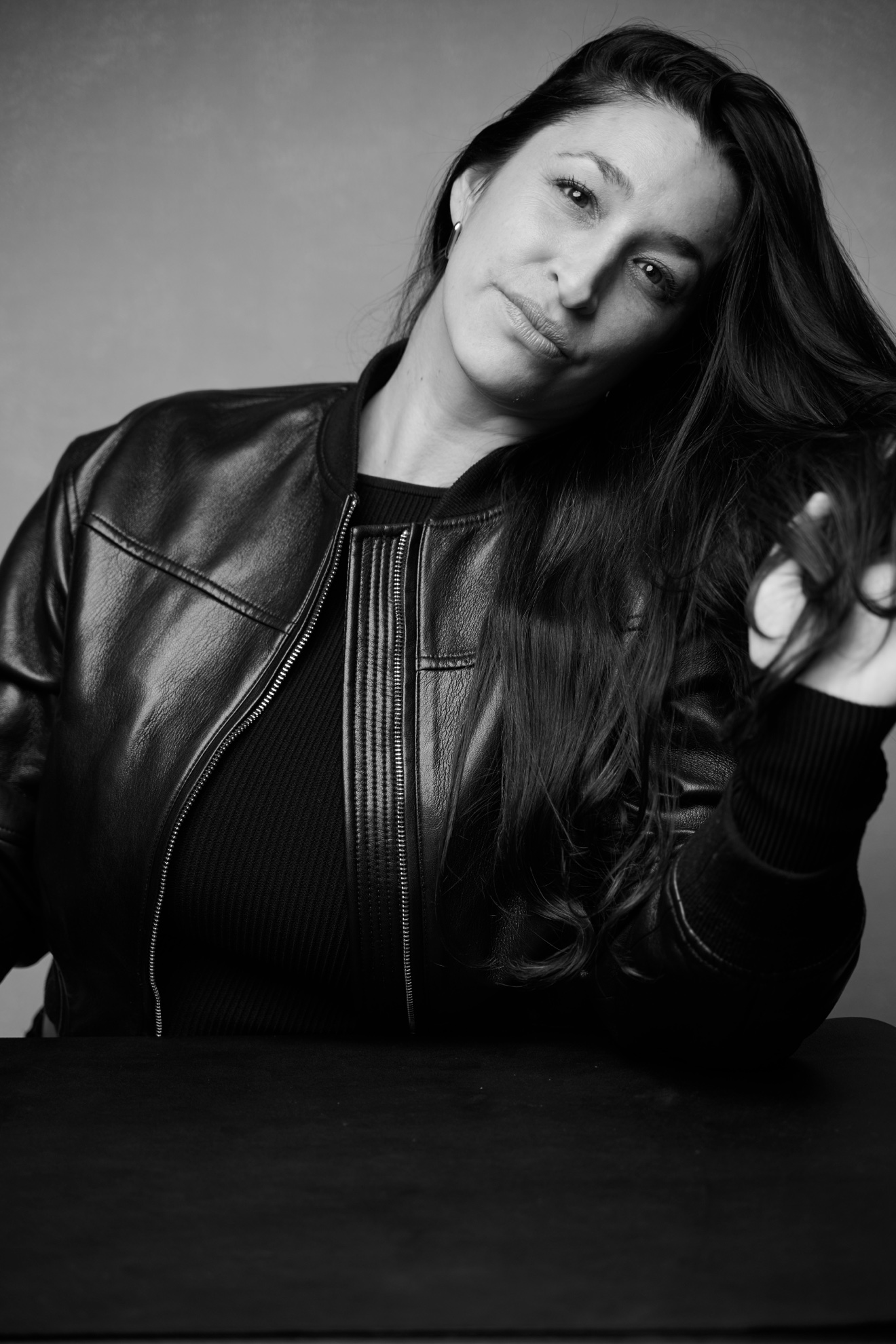 Black-and-white studio portrait of Sheefra Blumenthal in a leather jacket, head tilted with her hand in her hair